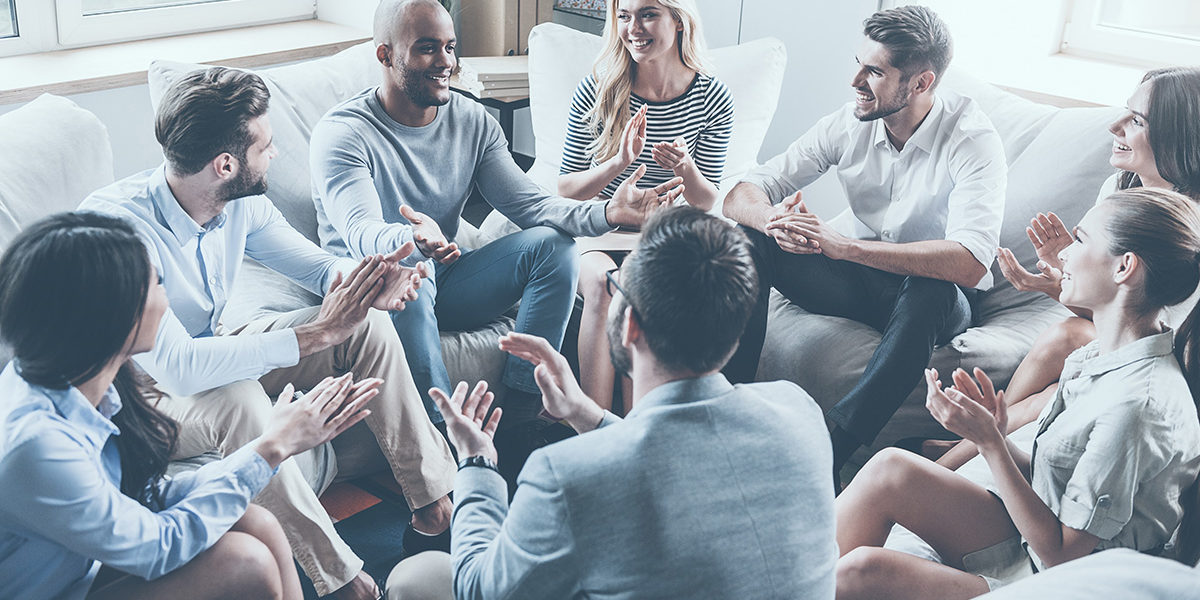 charateristics to look for in a sober living home people sitting in a therapy circle applauding a fellow patient